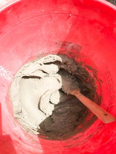 a red bucket filled with cement and a wooden spoon in the center, on top of it