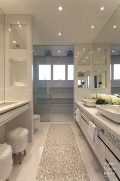 a white bathroom with two sinks, mirrors and stools in front of the bathtub