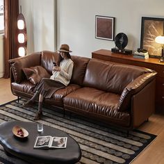 a person sitting on a brown leather couch in a living room with a table and lamp