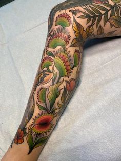 a woman's arm with tattoos on it and flowers in the middle, sitting on a bed