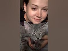 a woman holding a cat in her arms and looking at the camera with a smile on her face