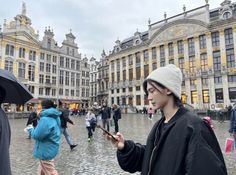 a woman holding an umbrella while looking at her cell phone in front of some buildings