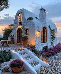 a house made out of rocks with plants and lights on the front door, along with steps leading up to it