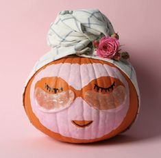 an orange pumpkin with eyes and a scarf on it's head, sitting in front of a pink background