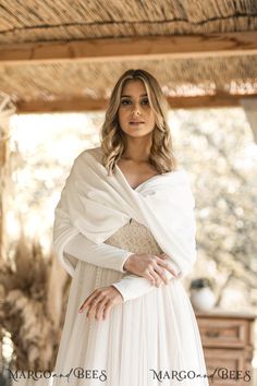 a woman wearing a white dress and shawl standing in front of a wooden structure