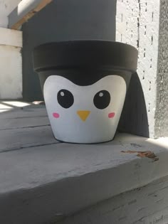 a small pot with a penguin face painted on the side of it, sitting on a ledge