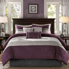 a bed with purple and white comforters in a bedroom next to two lamps on either side of the bed