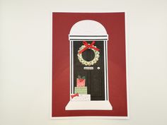 a red card with a black door and wreath on the front, sitting next to a white wall