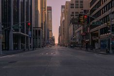 an empty city street with tall buildings and traffic lights in the distance at sunset or dawn