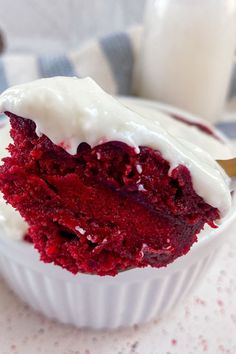 a piece of red velvet cake with white frosting in a cupcake dish next to a glass of milk