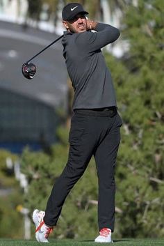 a man swinging a golf club on top of a green field