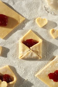 small pastries with jam in the middle on top of floured paper next to hearts