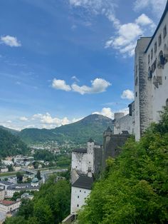 an old castle sits on top of a hill overlooking a town below it with mountains in the background