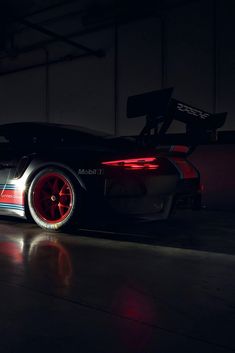 a black sports car with red rims parked in a dark garage, at night