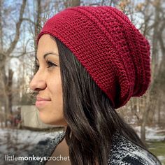 a woman wearing a red knitted hat in the winter with trees and snow behind her