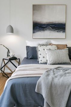 a bed with blue sheets and pillows in a bedroom next to a painting on the wall