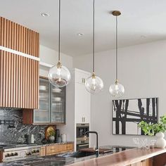 a kitchen with marble counter tops and hanging lights over the island in front of it