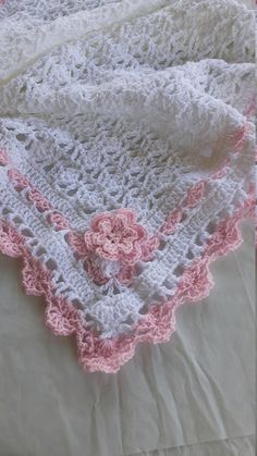 a white and pink crocheted blanket laying on top of a bed