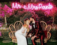 a man and woman are sitting on a bench in front of a pink neon sign