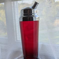 a red glass cup sitting on top of a window sill next to a white curtain