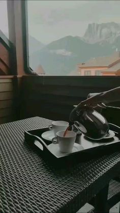 a person pours coffee into a cup on a tray with mountains in the background