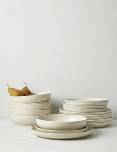 a stack of white plates and bowls with pears in the middle on a table