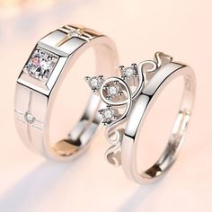 two wedding rings with princess crowns on each one and white diamonds in the middle, against a pink background