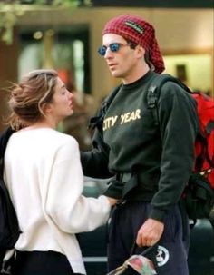 a man and woman standing next to each other with backpacks on their backs, talking