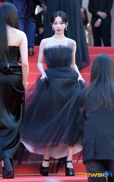 a woman in a black dress walking down the red carpet with other people behind her