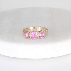 a three stone ring with pink and white stones on the sides, sitting on a marble surface