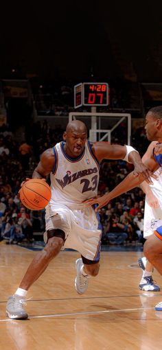 two men playing basketball on a court with people watching from the bleachers behind them