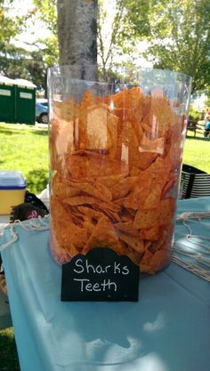 a jar filled with chips sitting on top of a table next to a sign that says shark's teeth