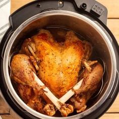 a slow cooker filled with cooked chicken and vegetables on top of a wooden table