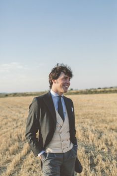 a man in a suit and tie is standing in a field smiling at the camera