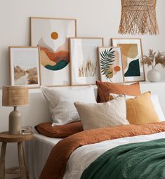 a bed topped with lots of pillows next to pictures on the wall and a lamp