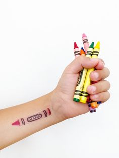 a person's arm holding several crayons in one hand and two on the other