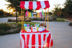 a red and white striped table topped with lots of candy on top of a sidewalk