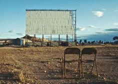 two empty chairs sitting in the middle of an empty field with a billboard behind them