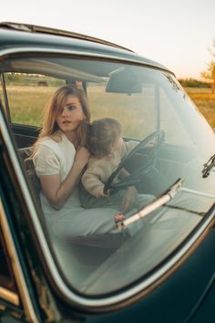 a woman sitting in the driver's seat of a car with her two children