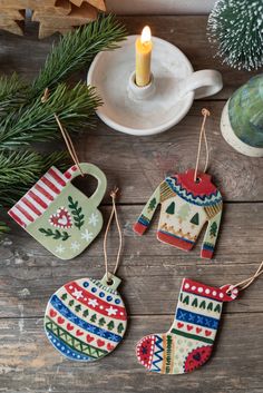 three christmas ornaments are hanging on a wooden table next to a candle and some pine branches