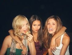 three beautiful young women standing next to each other in front of a dark background eating food