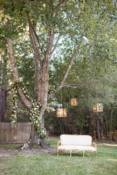 a white couch sitting under a tree next to a lush green field