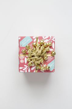 a gift wrapped in pink and gold wrapping paper with golden bows on top, sitting on a white surface