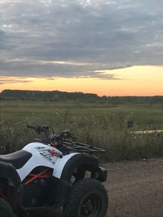 an atv parked on the side of a dirt road near grass and trees at sunset