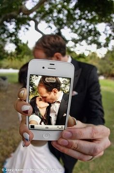 a person holding up a cell phone to take a picture with their wedding pictures on it