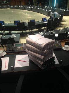 stacks of papers sitting on top of a table in front of an empty room filled with chairs