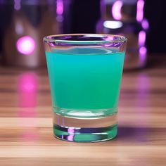 a glass filled with blue liquid sitting on top of a wooden table