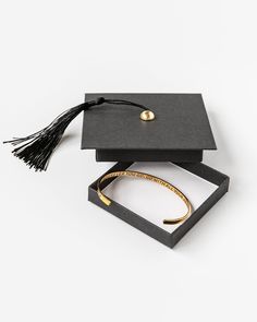 a graduation cap and tassel in a black box on a white surface with gold lettering