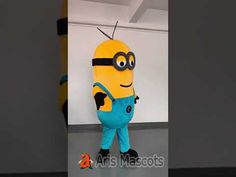 a yellow and blue minion mascot standing next to a white wall