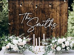 a table topped with white flowers and candles next to a wooden sign that says the smiths